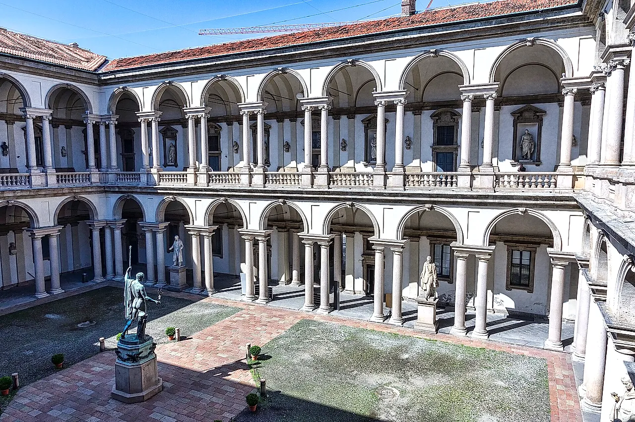 Der Hof des Palazzo Brera mit zwei Geschossen von Säulenarkaden aus hellem Stein, einer Bronzestatue auf einem Sockel im Vordergrund und einem Backsteinpflaster