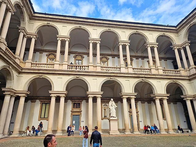 Der Hof des Palazzo Brera mit weißen Arkaden auf zwei Geschossen und einer weißen Statue auf einem Sockel in der Mitte; im Vordergrund stehen Besucher