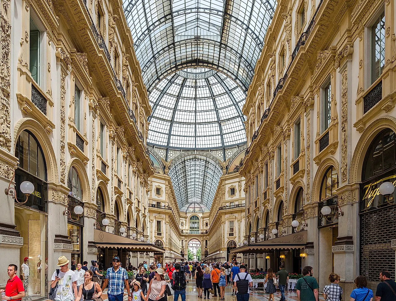 El interior de la Galleria Vittorio Emanuele II: la bóveda de cristal y hierro en lo alto, las fachadas ornamentadas con arcadas a ambos lados y multitudes de visitantes en primer plano.