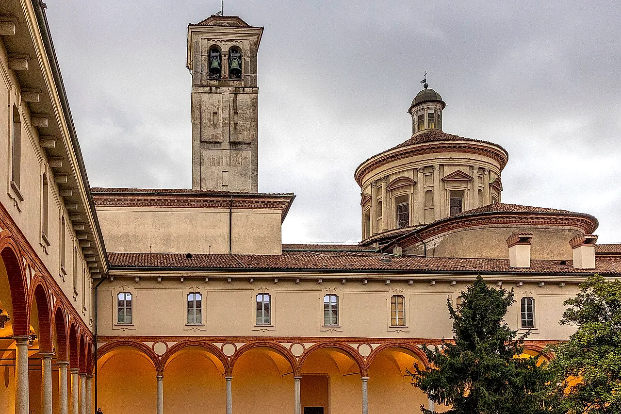 Il chiostro del museo della scienza: un edificio color crema con un loggiato illuminato da una luce calda a sinistra, e sullo sfondo un campanile e un tamburo cupolato sopra i tetti, sotto un cielo nuvoloso.
